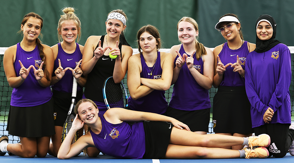 The 2023-24 Women's Tennis players pose, kneeling together, as one player stretches in front of them.